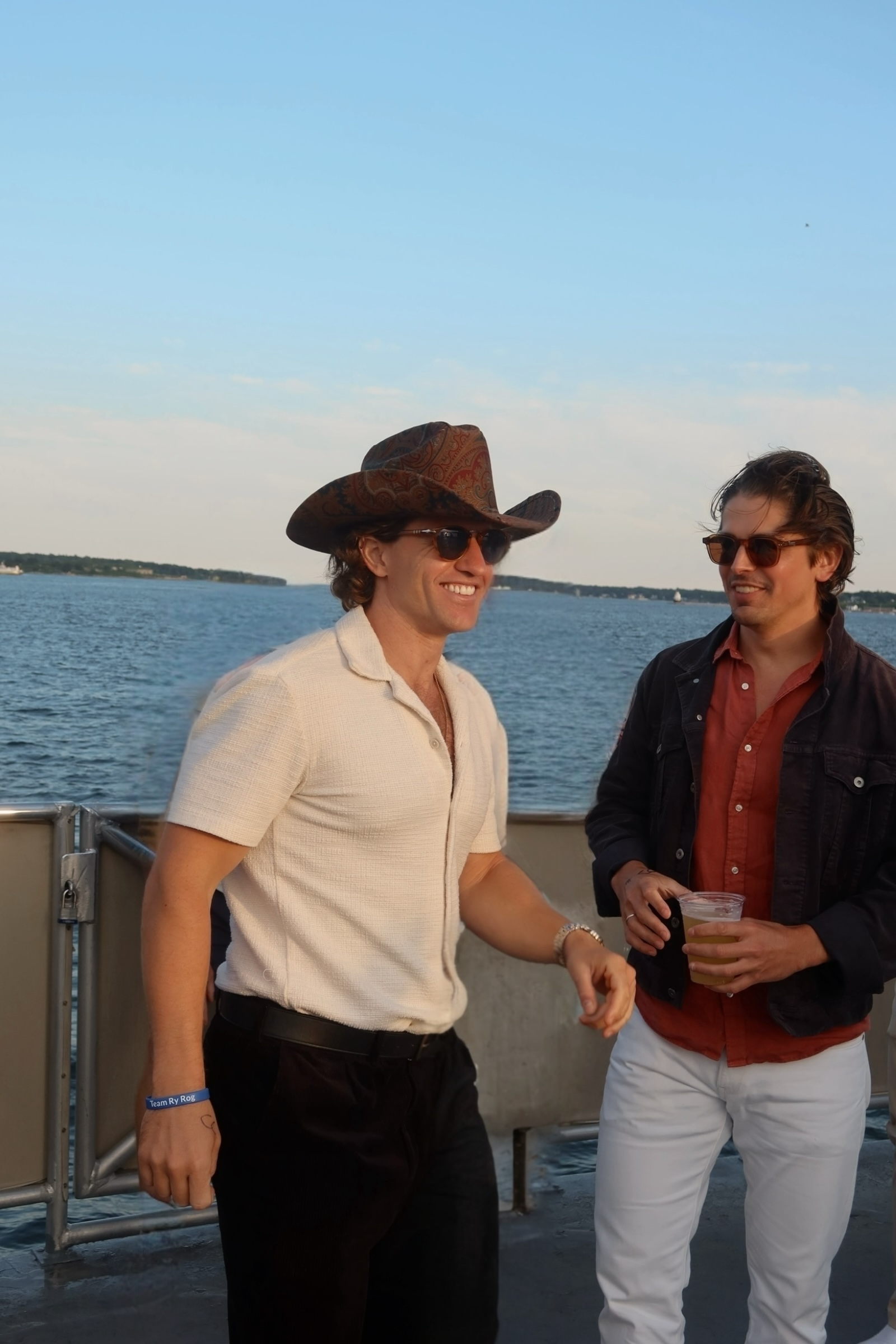 Two people standing on a dock by water, one wearing a cowboy hat.